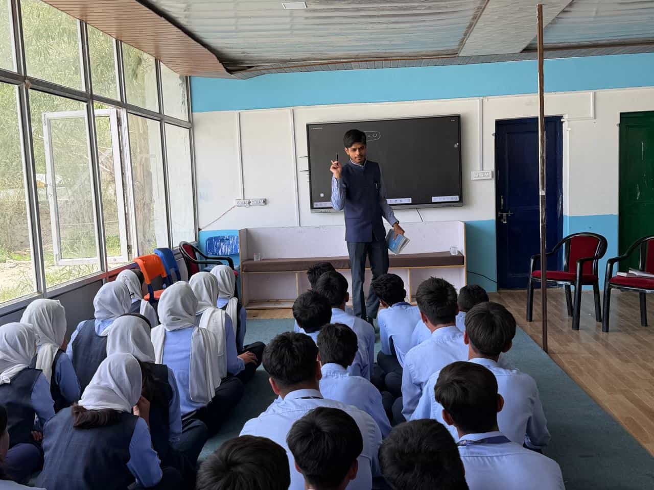 A teacher addressing students in a classroom fitted with a digital smart board